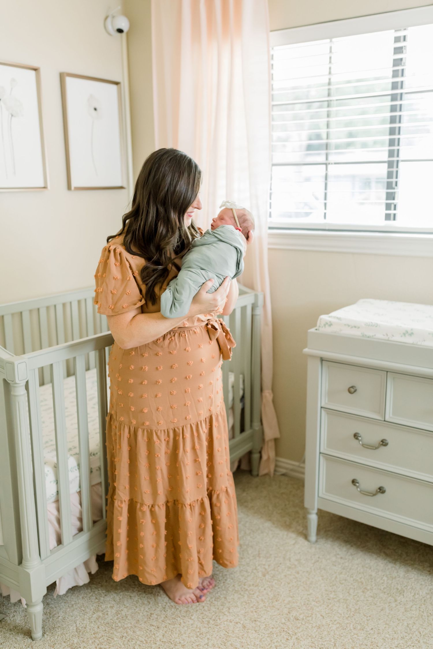 A peaceful moment in a neutral-toned nursery with vintage-style furniture and flowing curtains.