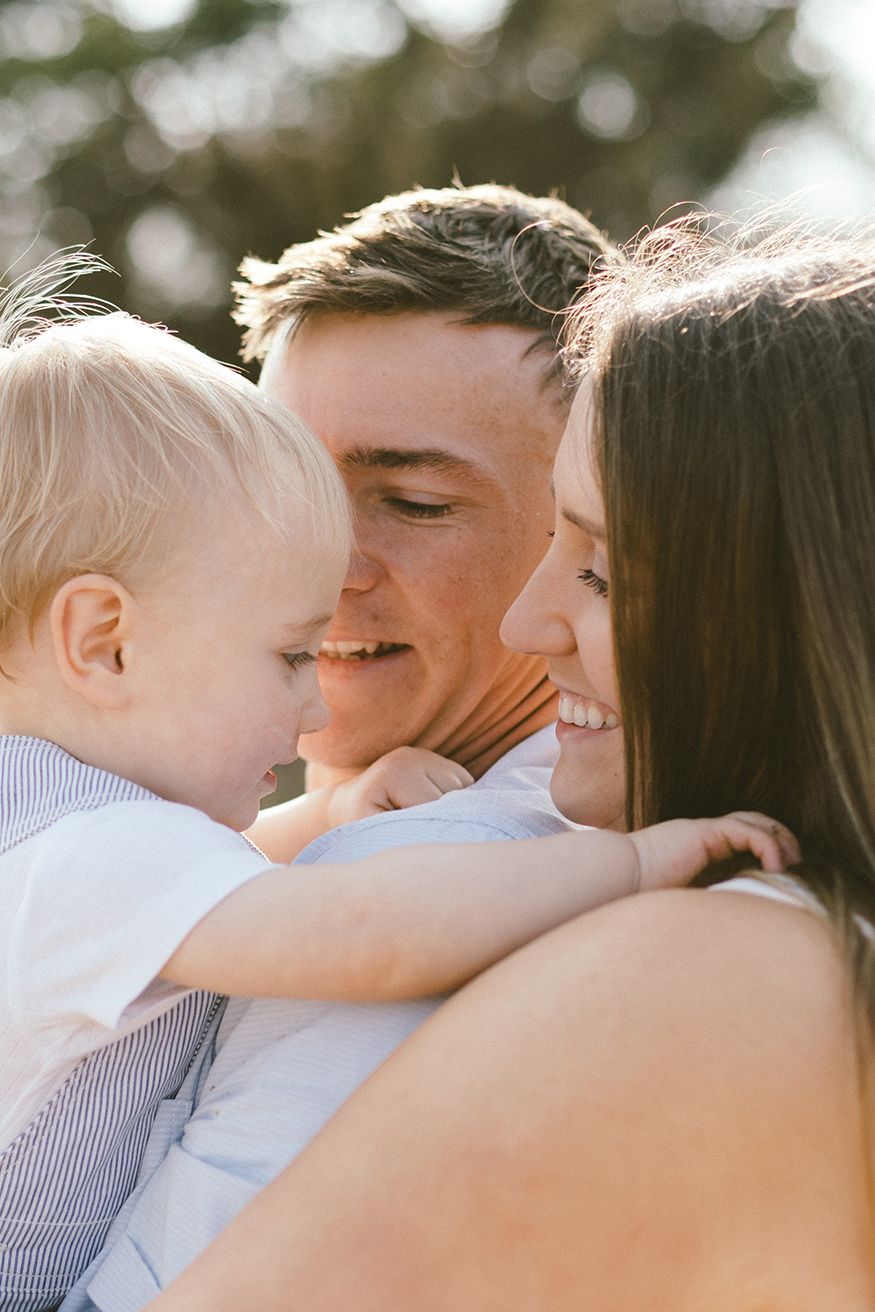 A tender family moment captured outdoors with warm sunlight filtering through the trees.