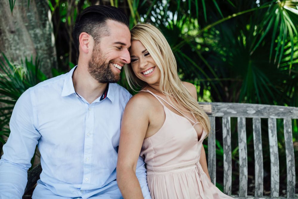 couple smiling at each other while she leans on his chest during an engagement session at Tropical Fairchild and gardens