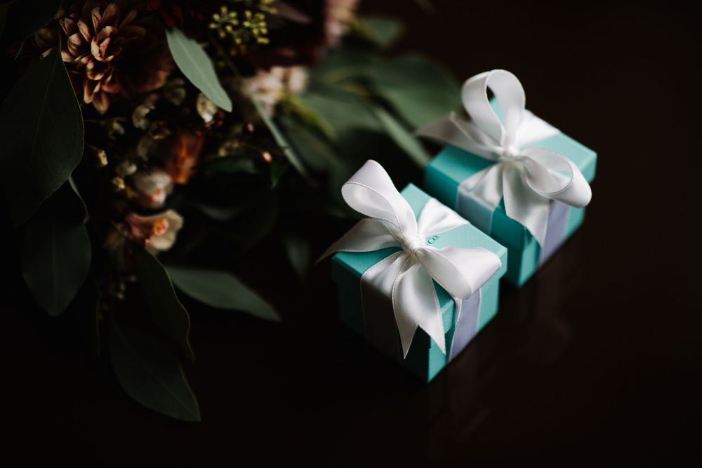 Two teal gift boxes with white bows against dark background with greenery.