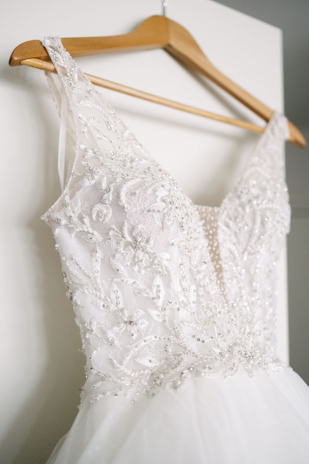 Close up of lace and beaded bodice detail on white wedding gown on wooden hanger.