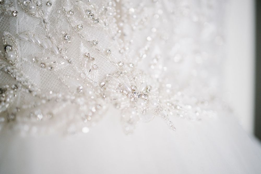 Macro shot of intricate beadwork details on white wedding dress fabric.