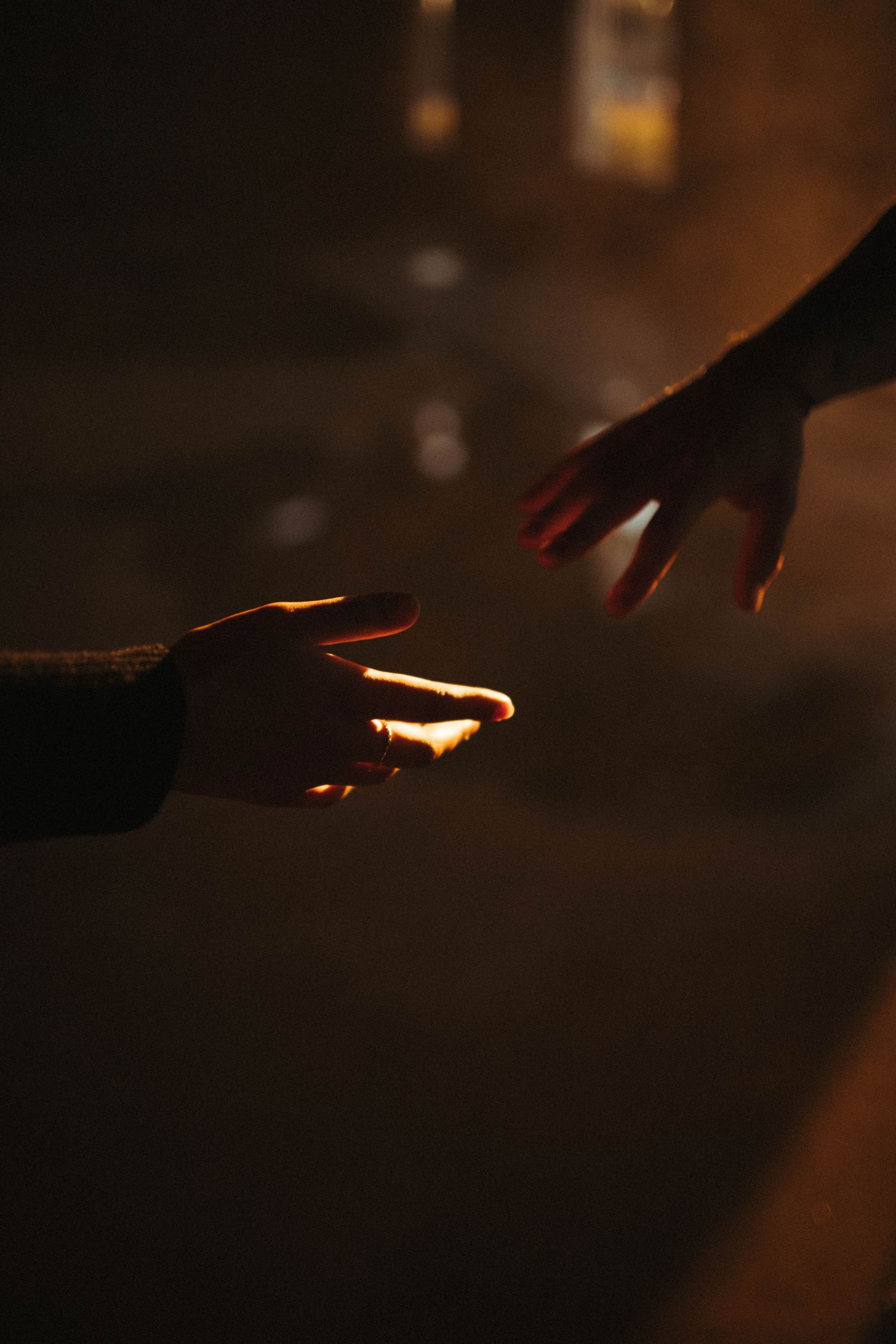 Silhouette of two hands reaching towards each other in dim lighting.