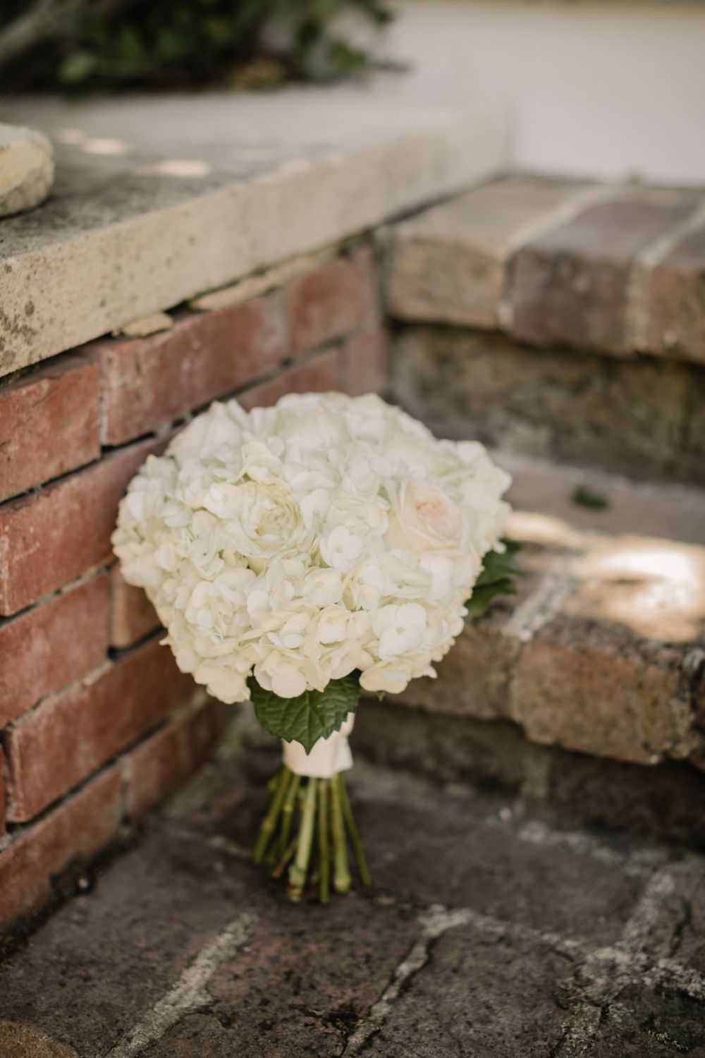 Classic white rose and hydrangea bridal bouquet resting on brick steps.