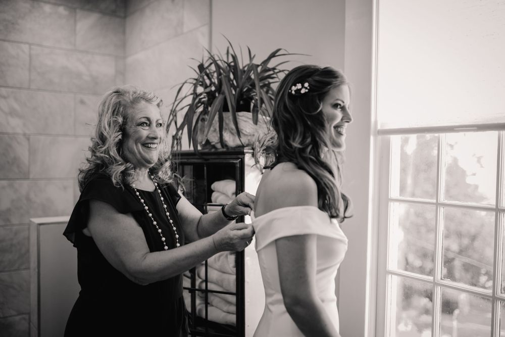 Black and white candid moment of wedding preparation in a sunlit room.