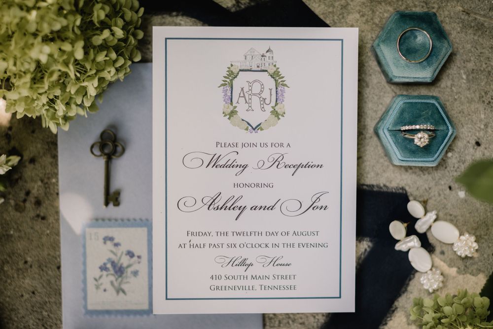 Wedding invitation with navy and teal accents featuring a monogram crest design and vintage key.