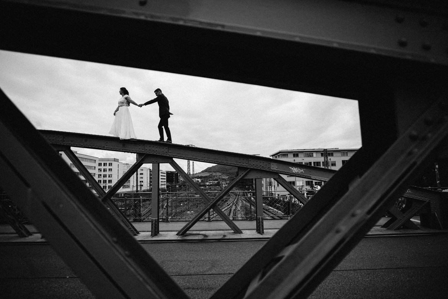 Silhouettes stand atop bridge beams in dramatic black and white urban composition.