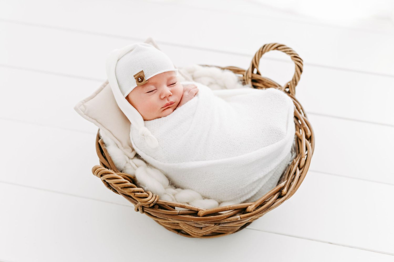 Sleeping newborn baby wrapped in white blanket lying in woven basket.