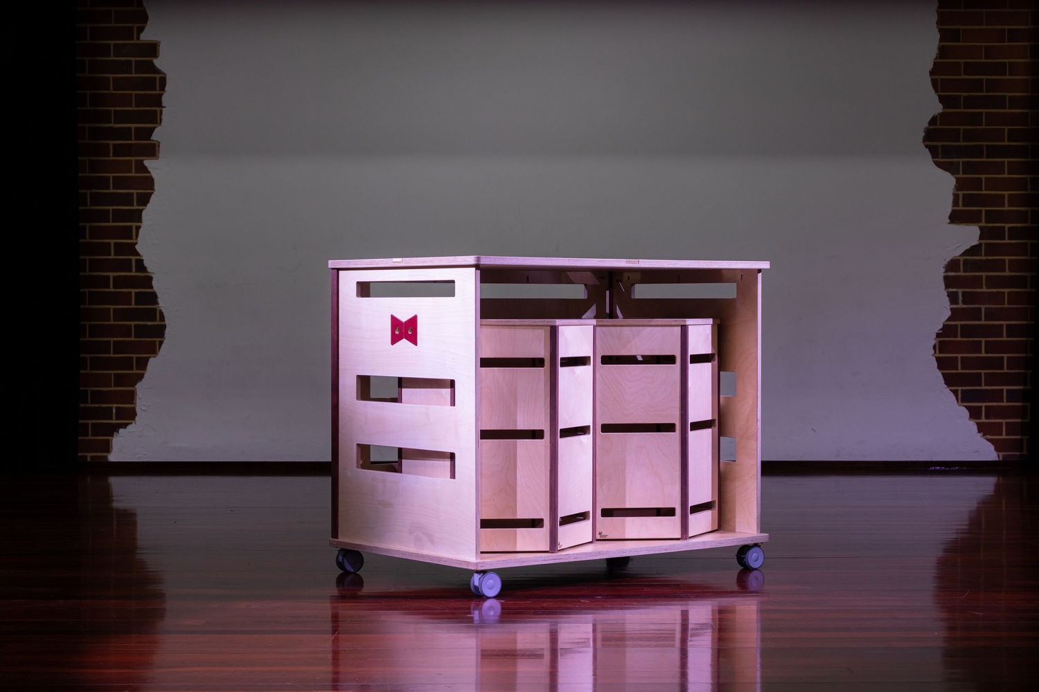 Pink-lit modern storage cabinet on wheels with multiple compartments against a dark wall.