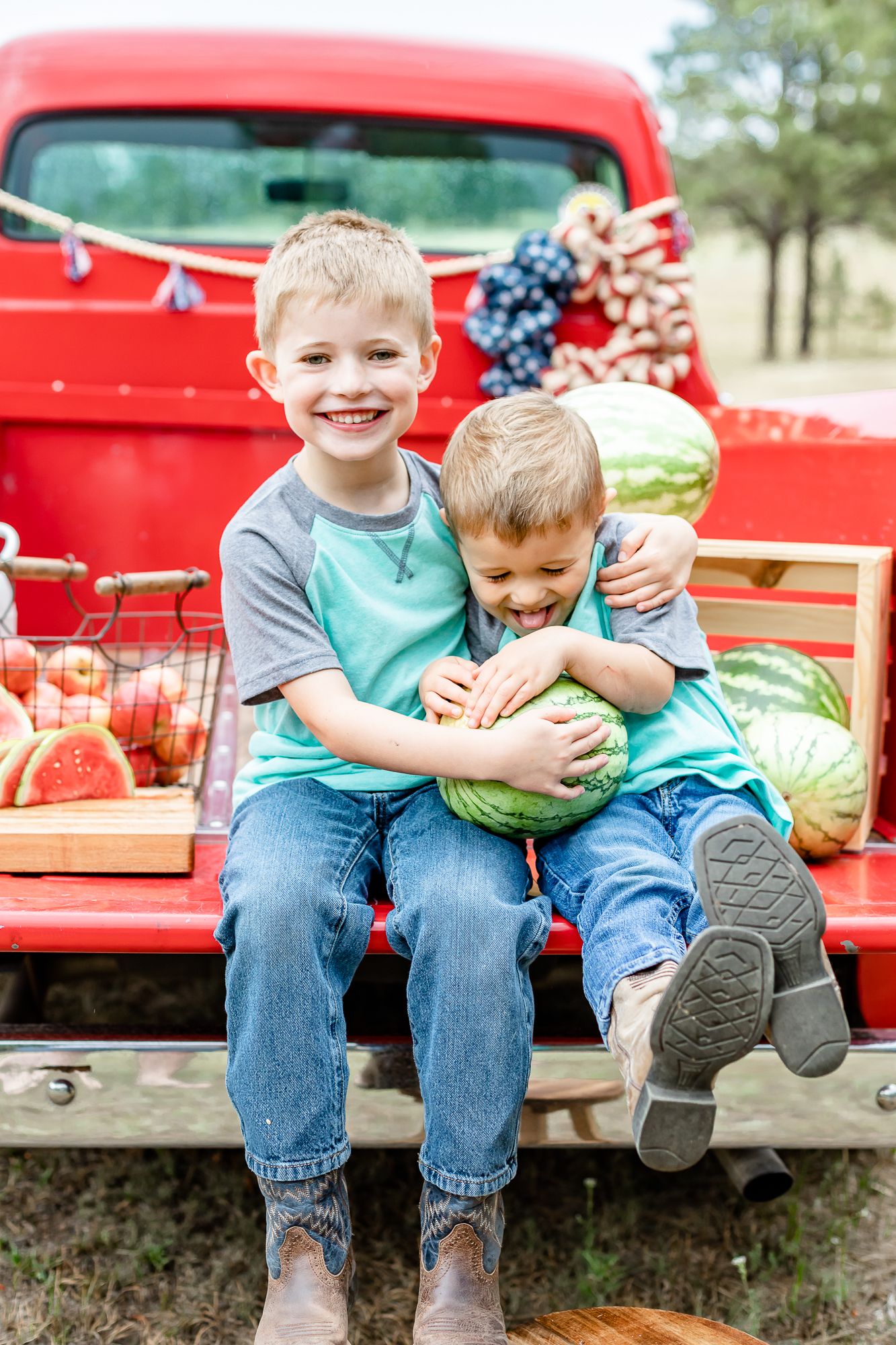 Two brothers sit in a red truck hold a watermelon and giggle in Colorado Springs, Colorado.