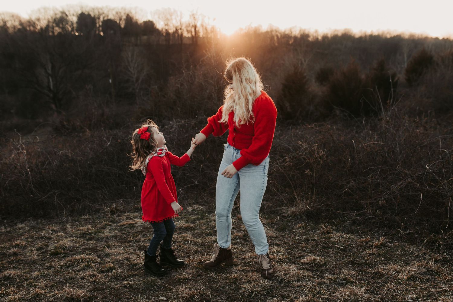 Two people in red clothing hold hands while walking in a field at sunset.