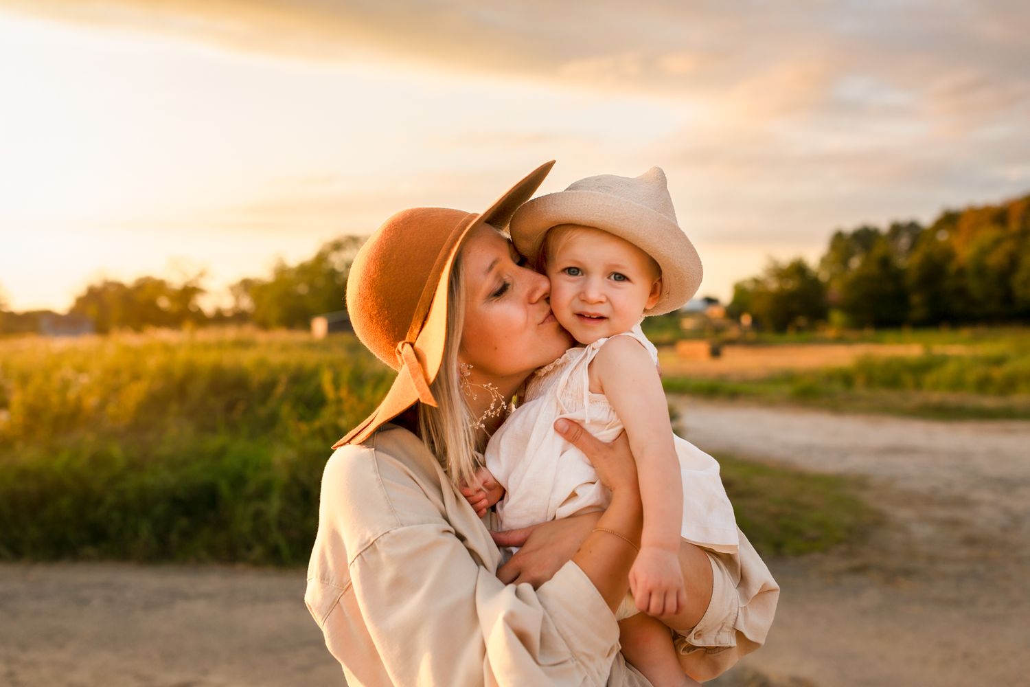 Parent and child in light colored clothing sharing tender moment outdoors during sunset.