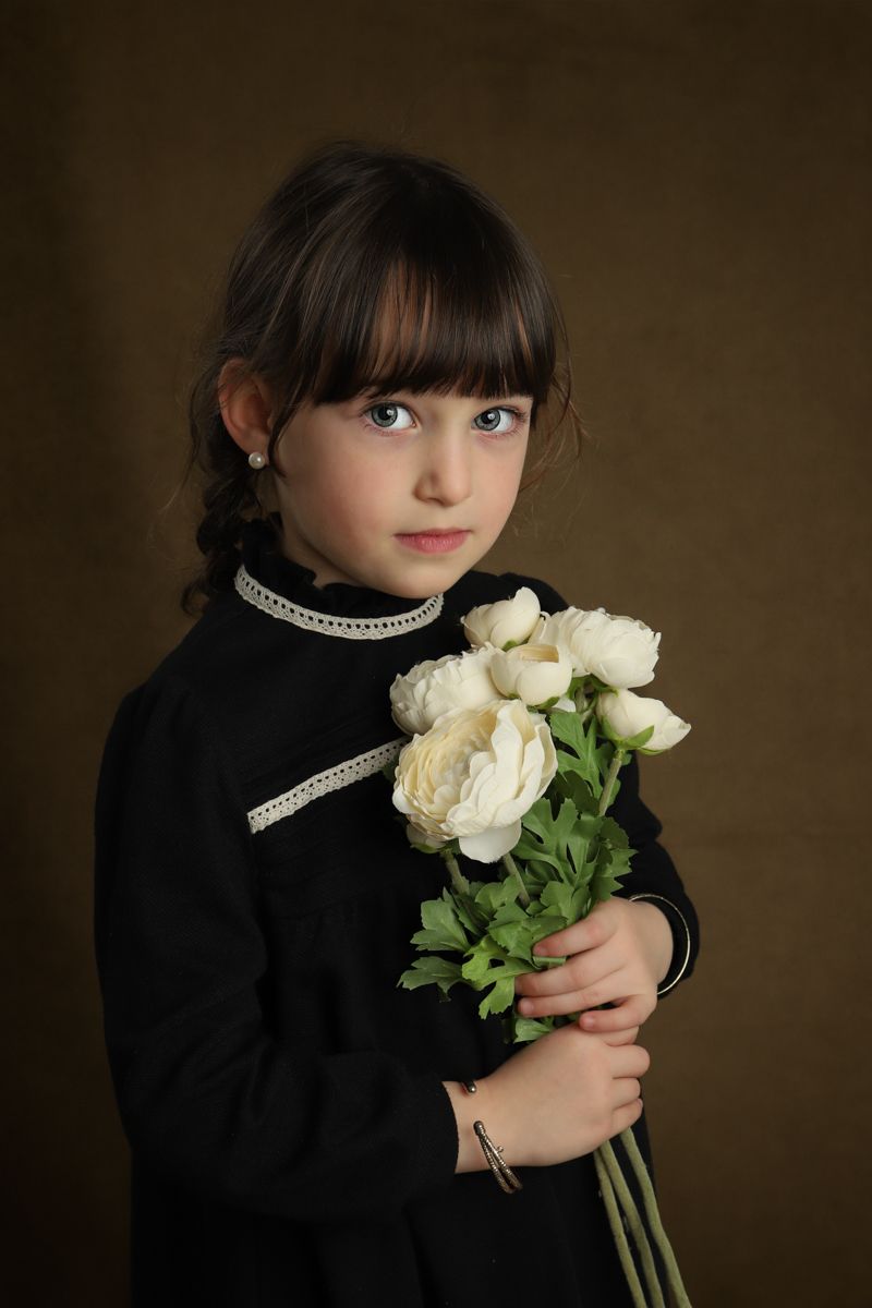 A classic portrait featuring a dark-haired youth in black holding white roses against a brown backdrop.