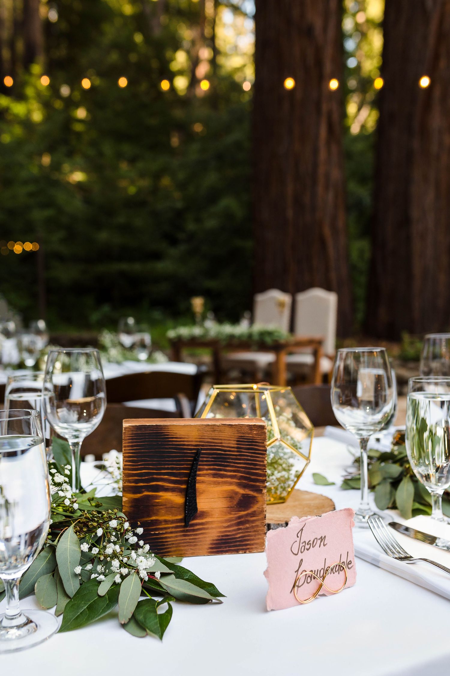 Rustic wooden table number with white floral arrangements and wine glasses at outdoor reception.
