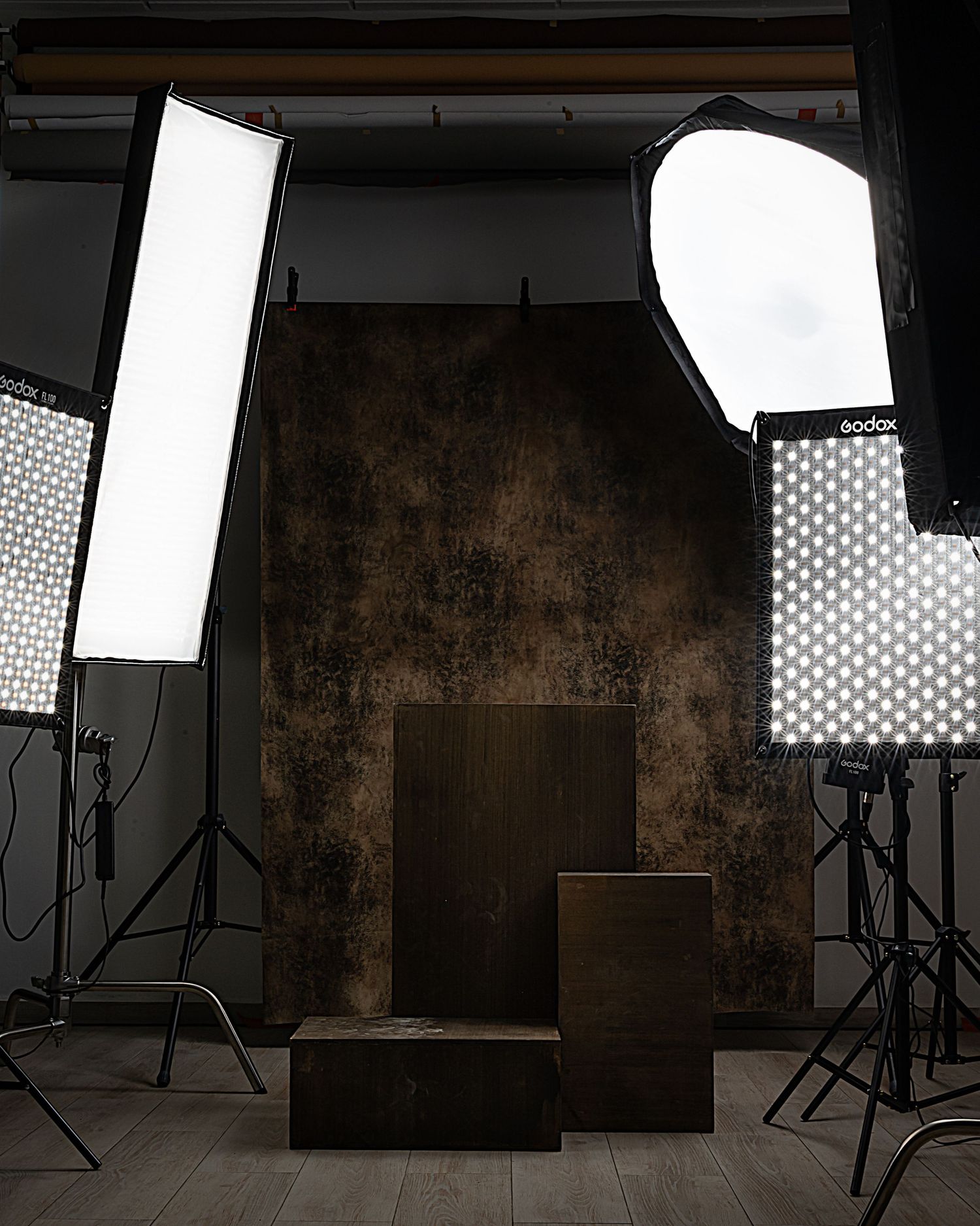 Photography studio interior with multiple lighting setups and softboxes arranged against dark walls.