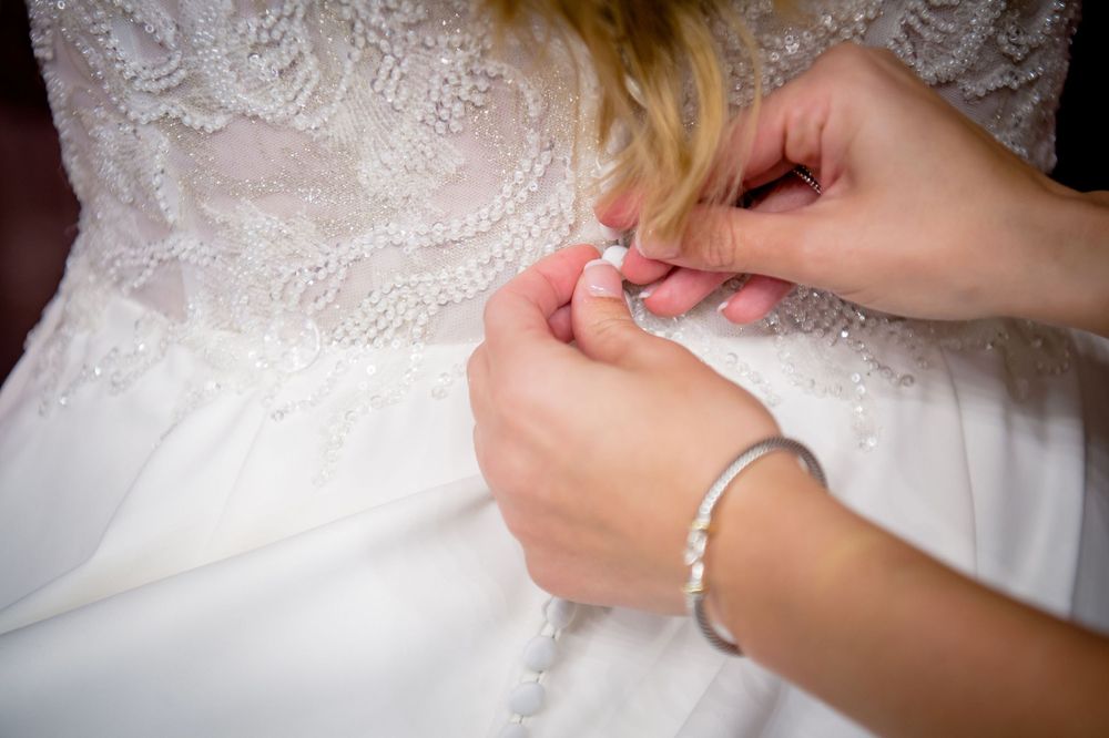 Close-up detail of hands adjusting white lace on wedding dress.
