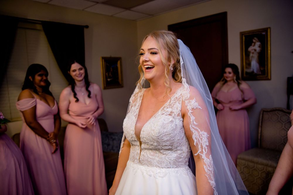 Person in white wedding gown and veil standing with bridesmaids in pink dresses.