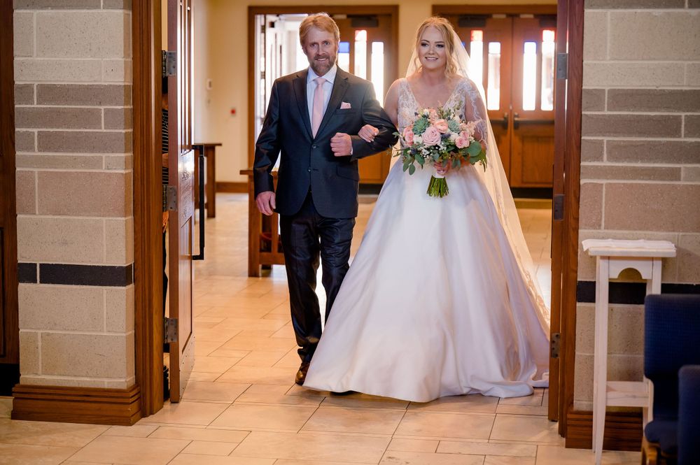 A couple walks down a church hallway during a wedding ceremony procession.