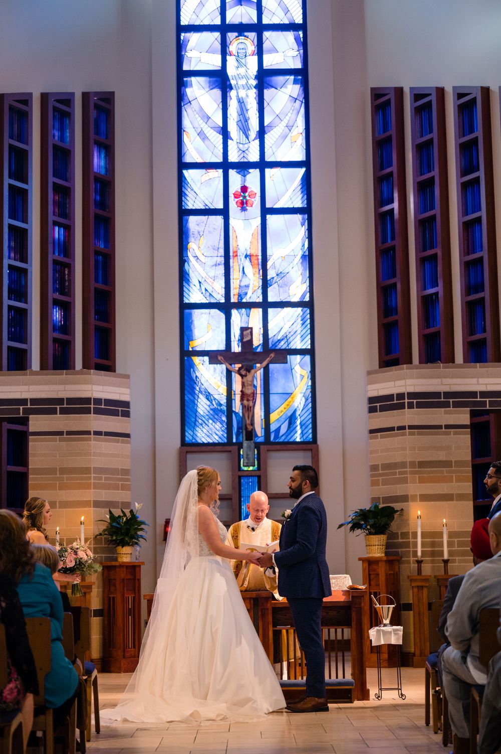 A religious wedding ceremony taking place in a church with a tall stained glass window.