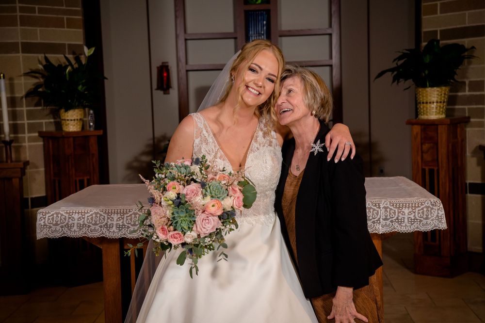 Two wedding guests share a joyful moment while posing for a photo in a church.