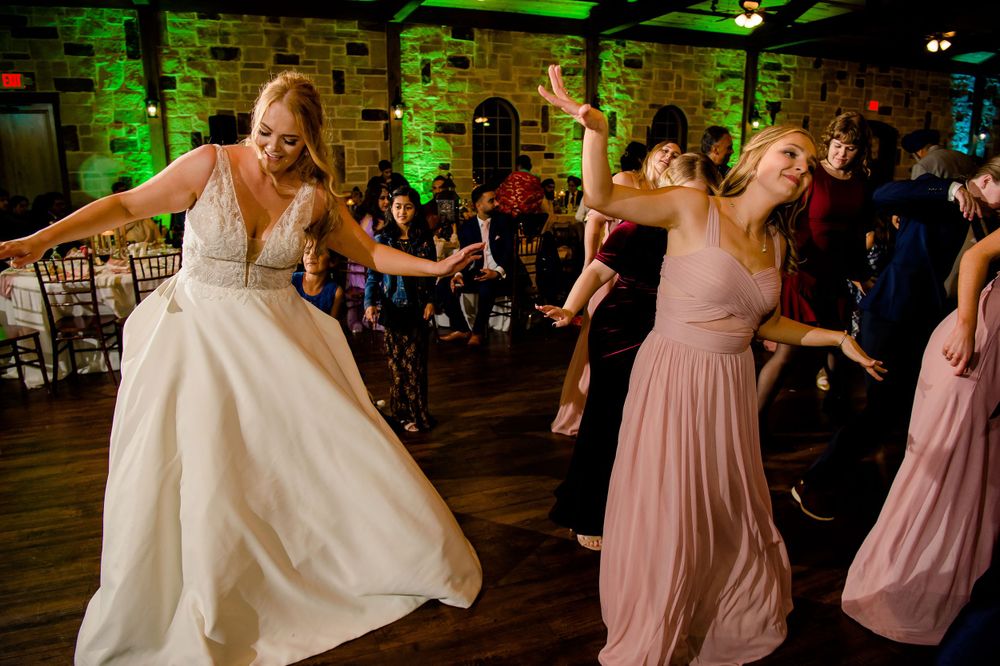 Wedding celebration with dancers in white and pink dresses moving energetically on a rustic dance floor.