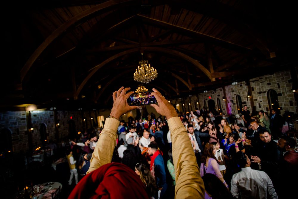 Guest capturing photo of dance floor celebration with phone at wedding reception.