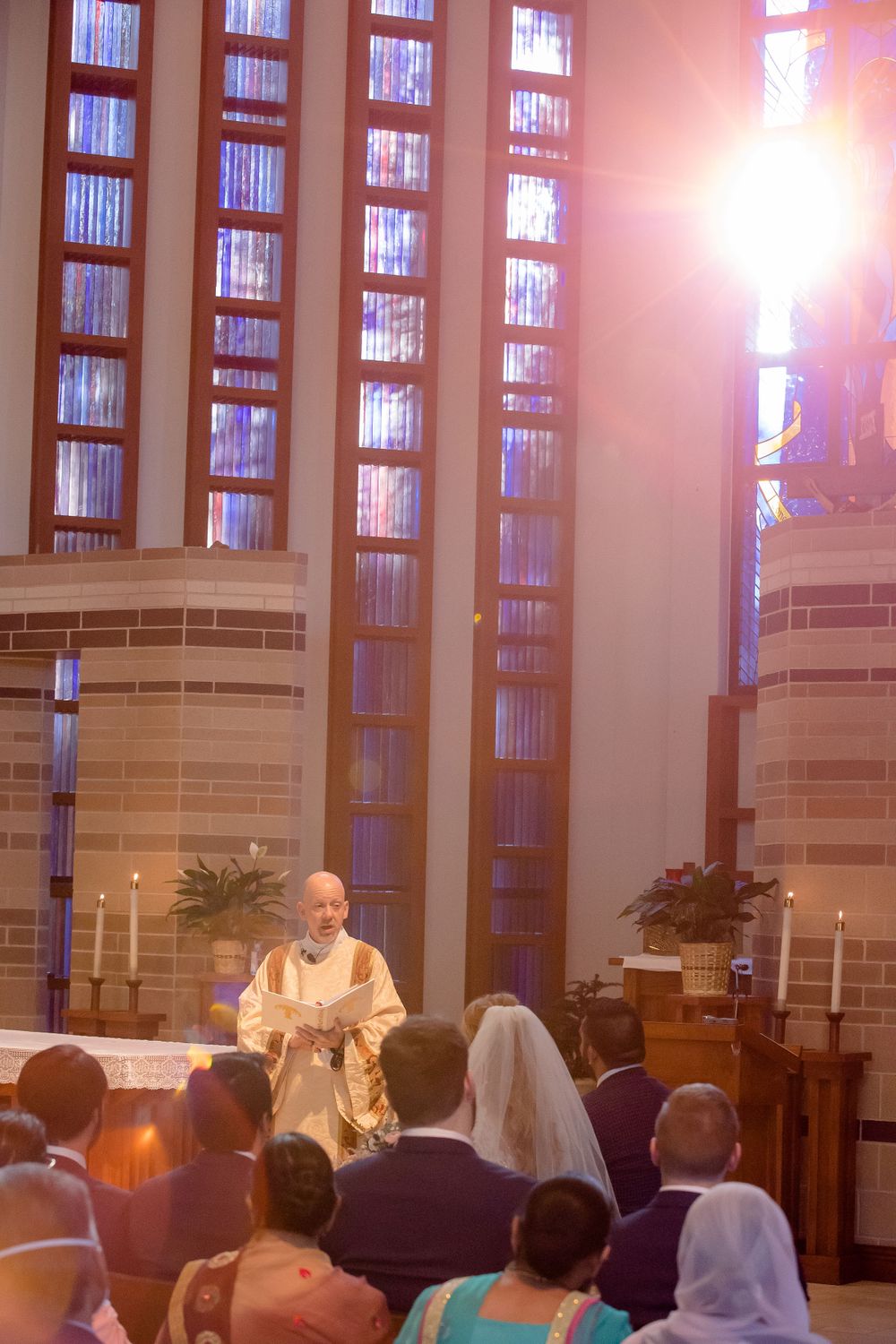 A religious ceremony takes place in a church with tall windows and sunlight streaming through during a wedding service.
