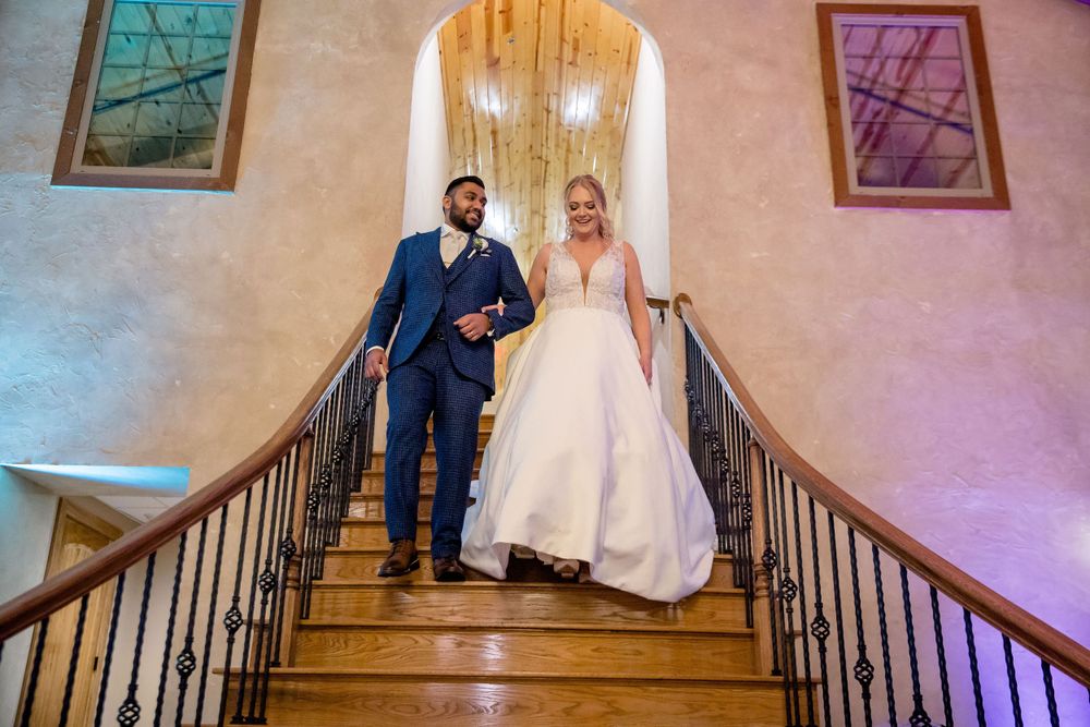 A couple descends an elegant staircase in wedding attire at their ceremony venue.
