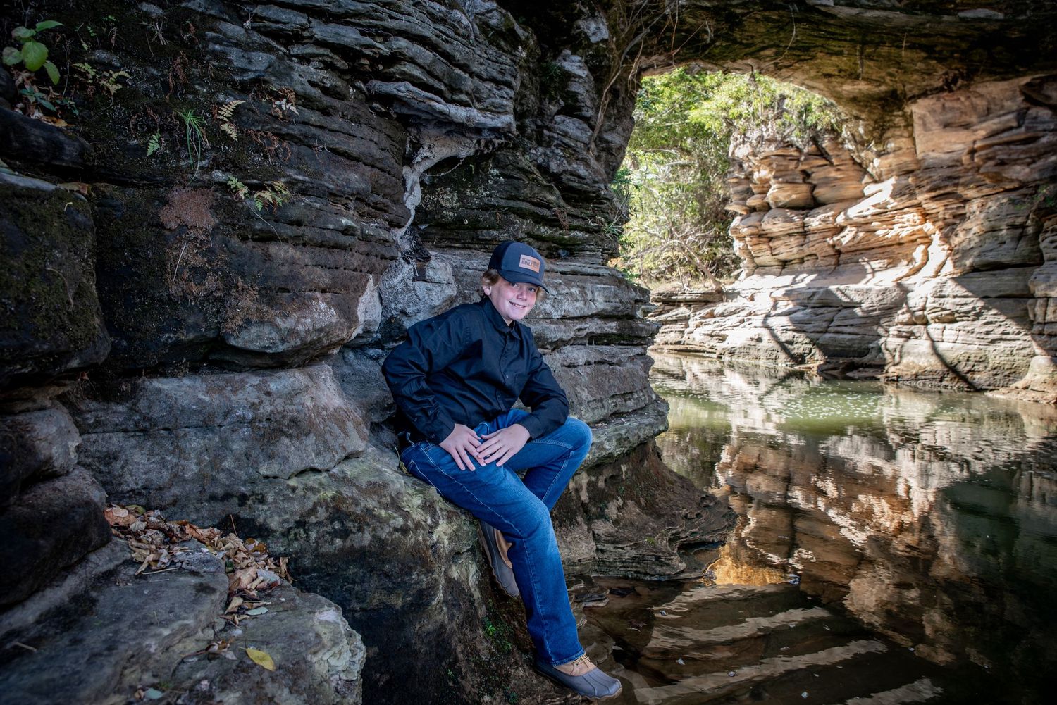 Person sitting in natural rock cave formation with dramatic lighting and shadows.