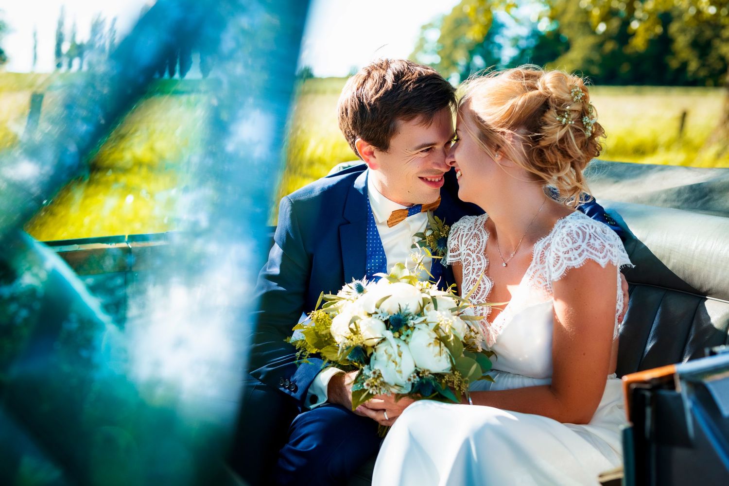 Romantic wedding portrait of a couple with white bouquet through blue-tinted glass.
