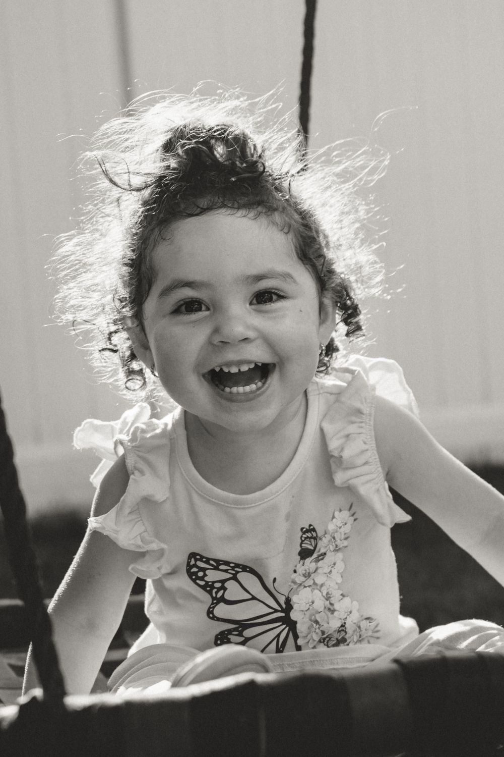 Black and white portrait of a child with windswept hair laughing with pure joy.