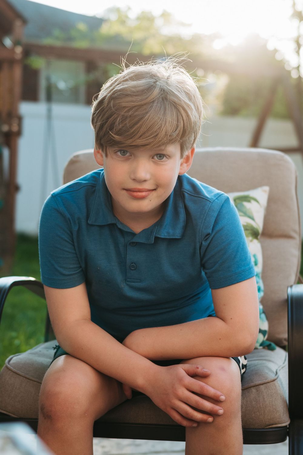 Young person in teal polo shirt sitting on patio furniture at sunset.