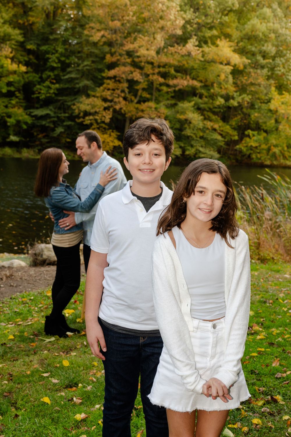 Family members in white and casual attire posing together outdoors during fall photo session.