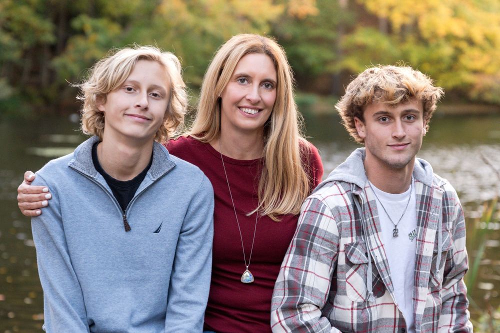 Family group posing together by lake with autumn foliage in background.