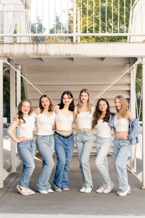 High School Dance Team in coordinated outfits with white tops and blue jeans pose together outdoors on campus.