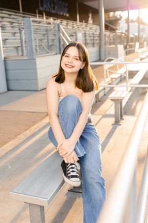 Casual dancer portrait on bleachers at sunset with blue jeans and black sneakers as golden light streams across metal benches.