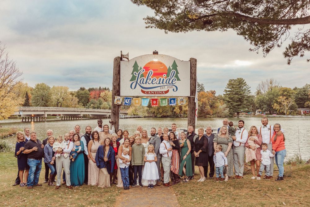 Wedding group photo with guests lined up under rustic park entrance during fall season.