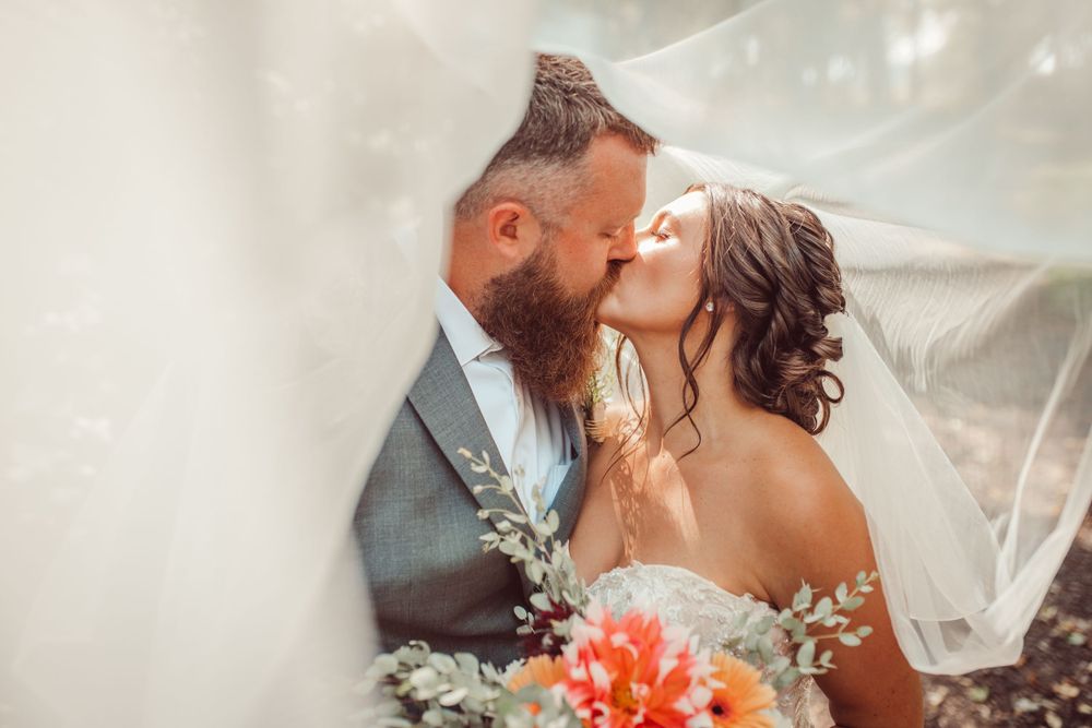 Romantic wedding portrait with flowing veil and coral bouquet.