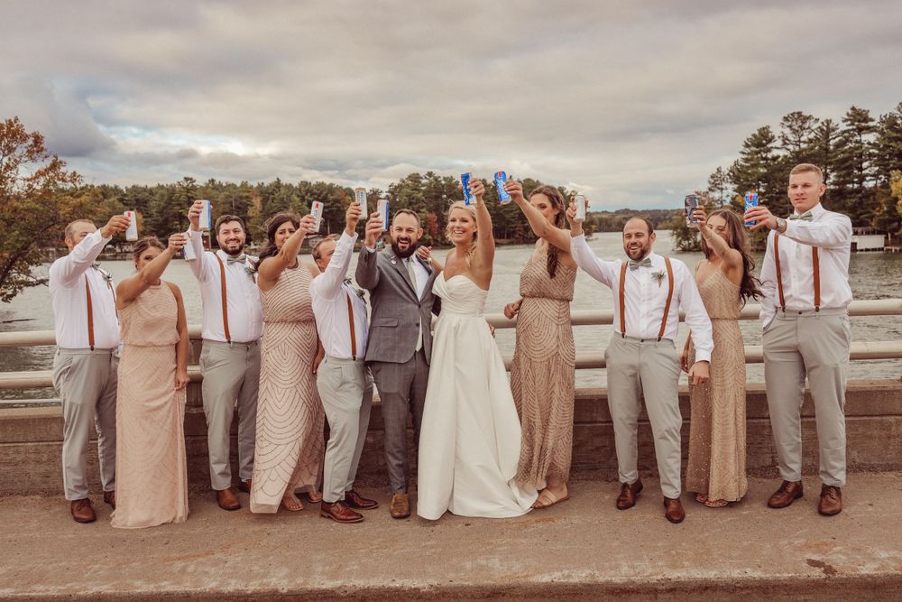 Wedding party in neutral tones poses together outdoors on a cloudy day.