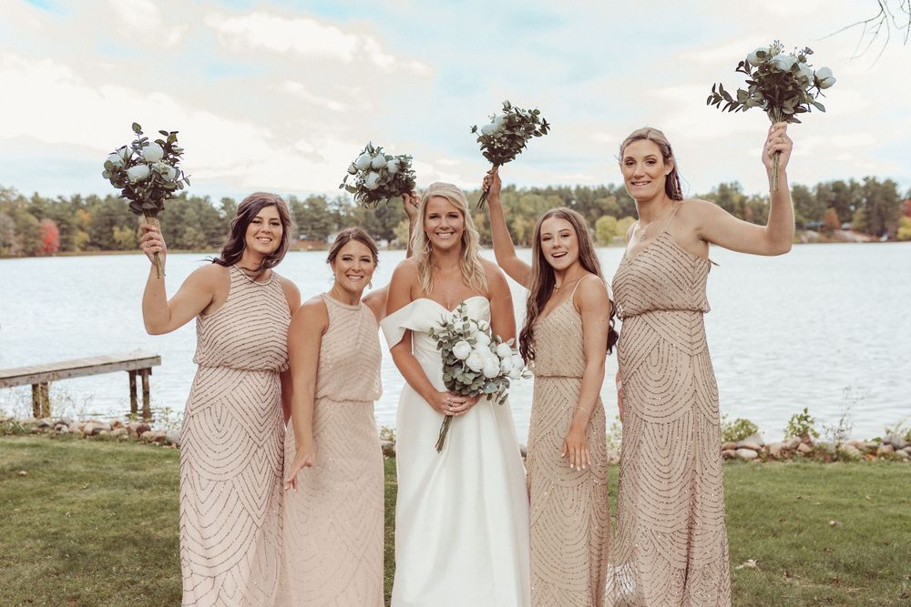 Wedding party in blush dresses poses with bouquets by lakeside.