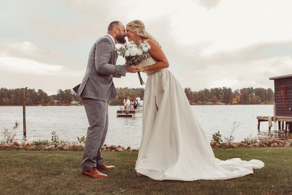 Couple shares intimate moment by lakeside during sunset wedding celebration.