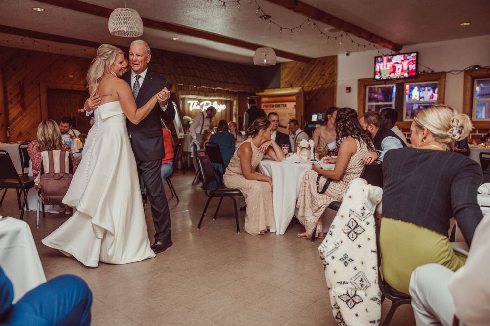 Newlyweds share first dance in reception hall while guests watch from decorated tables.