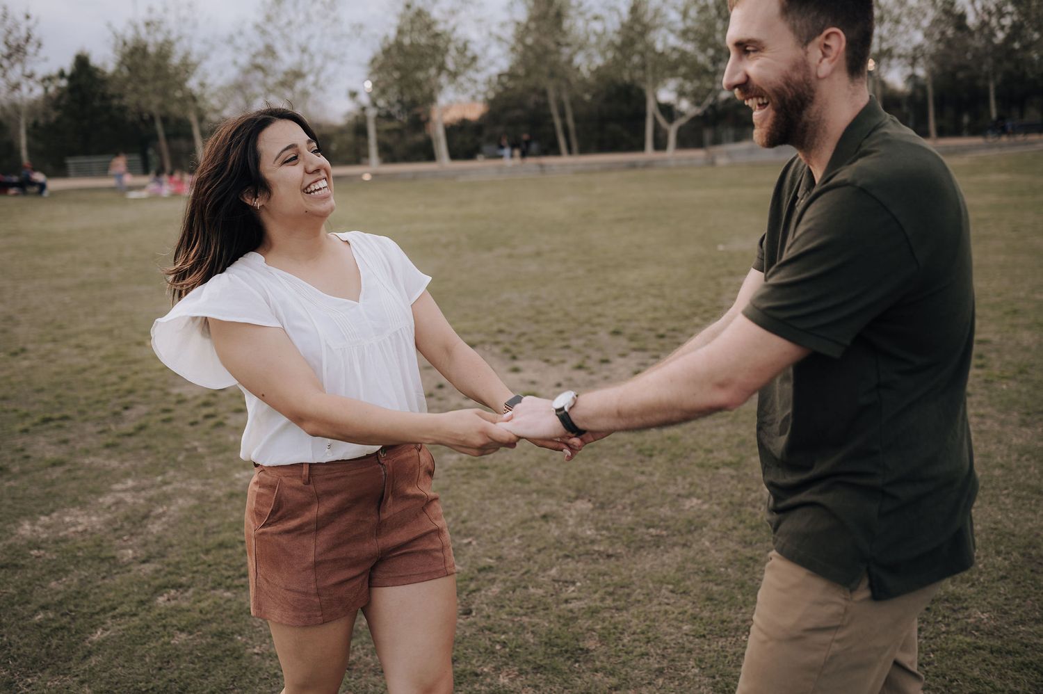 A joyful couple holding hands and dancing together in a park setting.