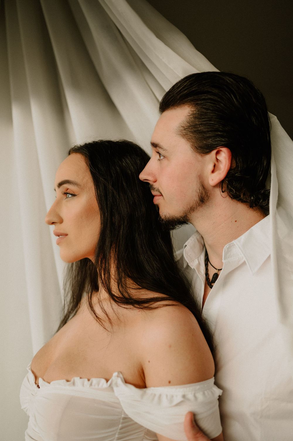 Romantic couple photoshoot with soft white drapery in the background creating an intimate atmosphere.
