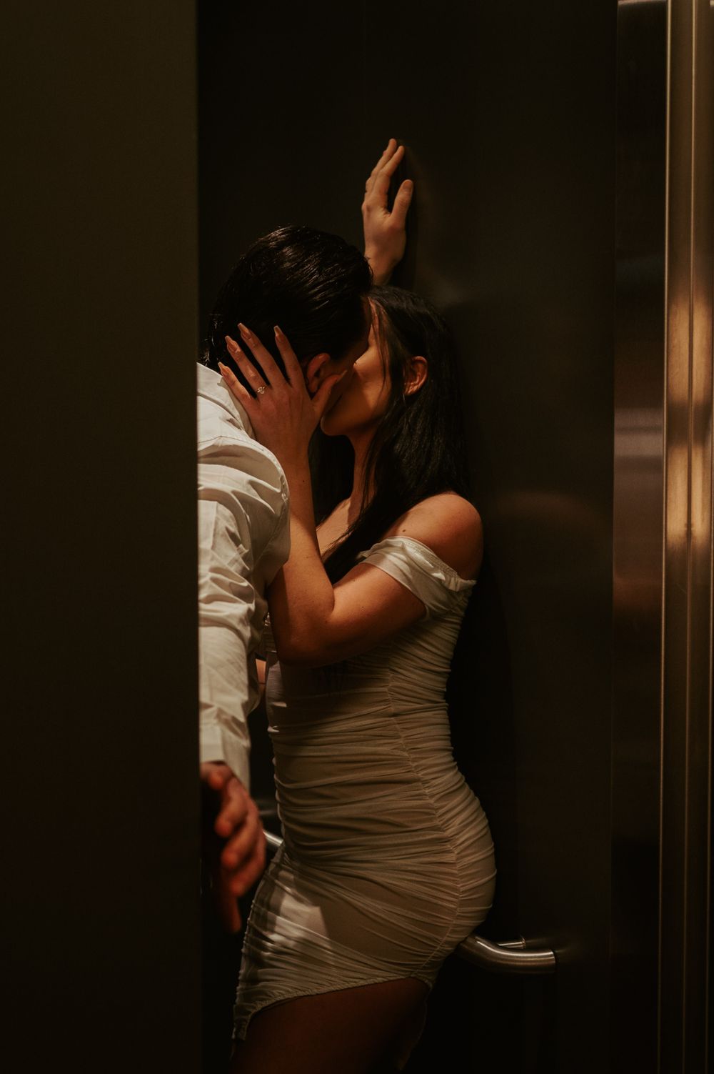 Dramatic lighting captures intimate moment near elevator.