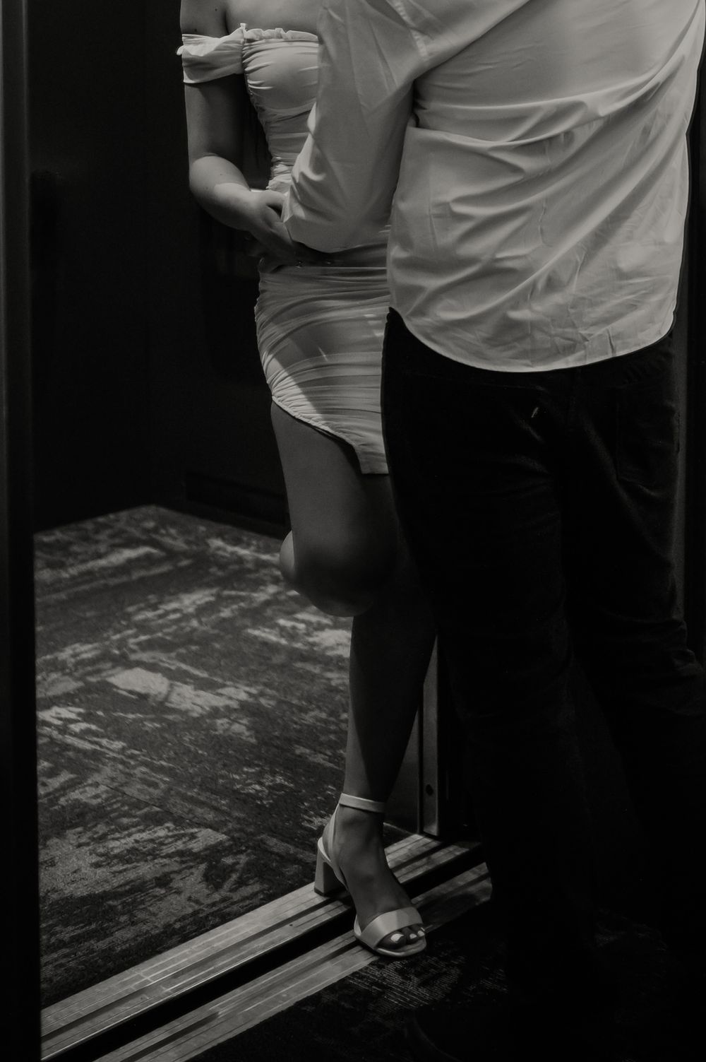 Two people standing near elevator doors in low light.