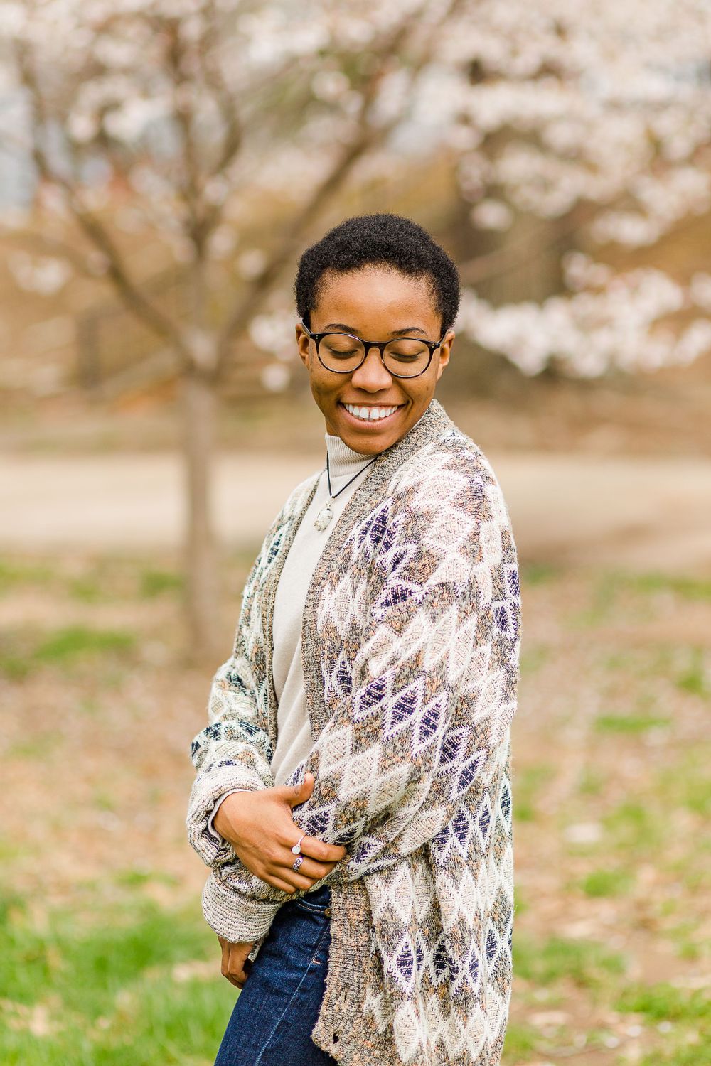 Portrait against blooming trees wearing patterned cardigan and classic casual wear.
