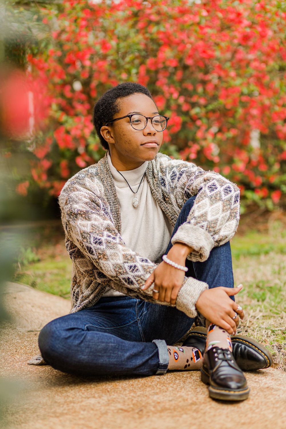 Casual outdoor portrait with patterned sweater against vibrant red flowering bush.