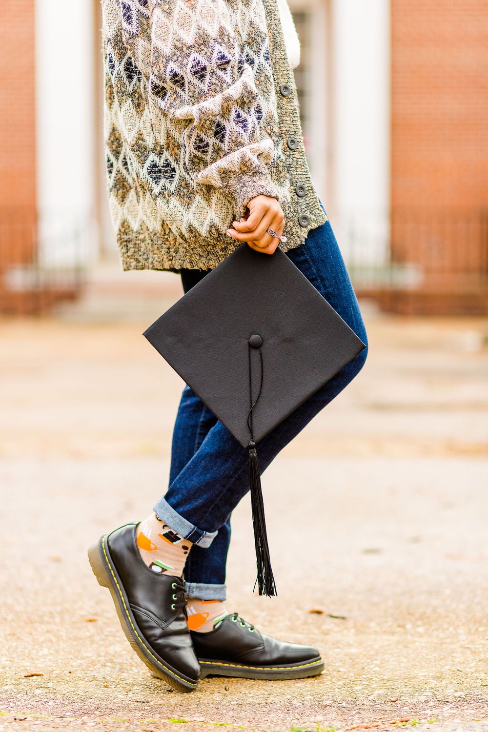 Graduation detail shot showing mortarboard, cardigan sleeve, and black dress shoes.