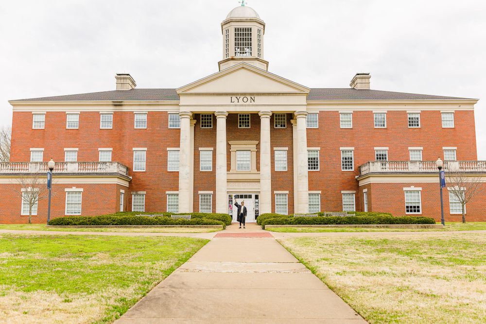 Classic red brick university building with white columns and cupola under cloudy sky.